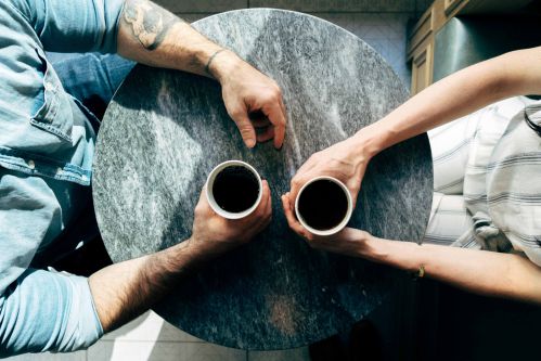 maos de duas pessoas sobre uma mesa segurando um café como se conversassem