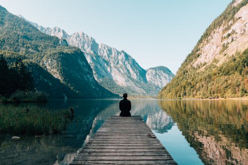 Homem sentado sozinho olhando para água no meio de uma linda paisagem