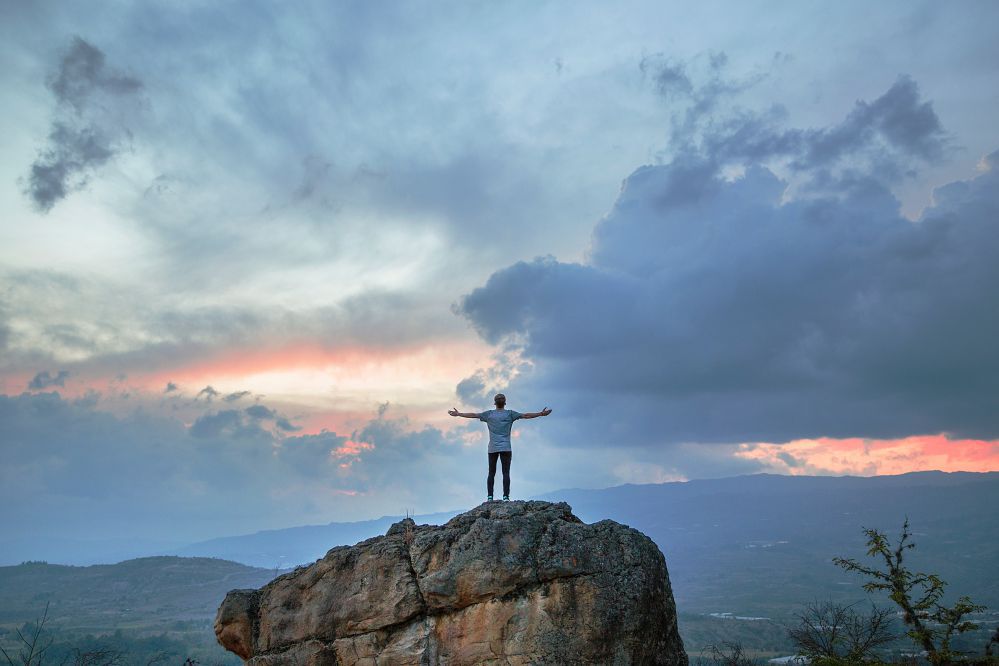 Homem de braços abertos no topo de uma pedra